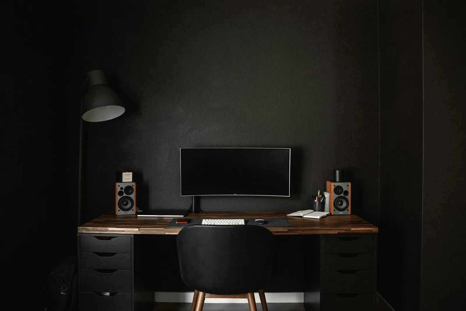 Escritorio ordenado con un monitor, parlantes y una lámpara en una habitación oscura