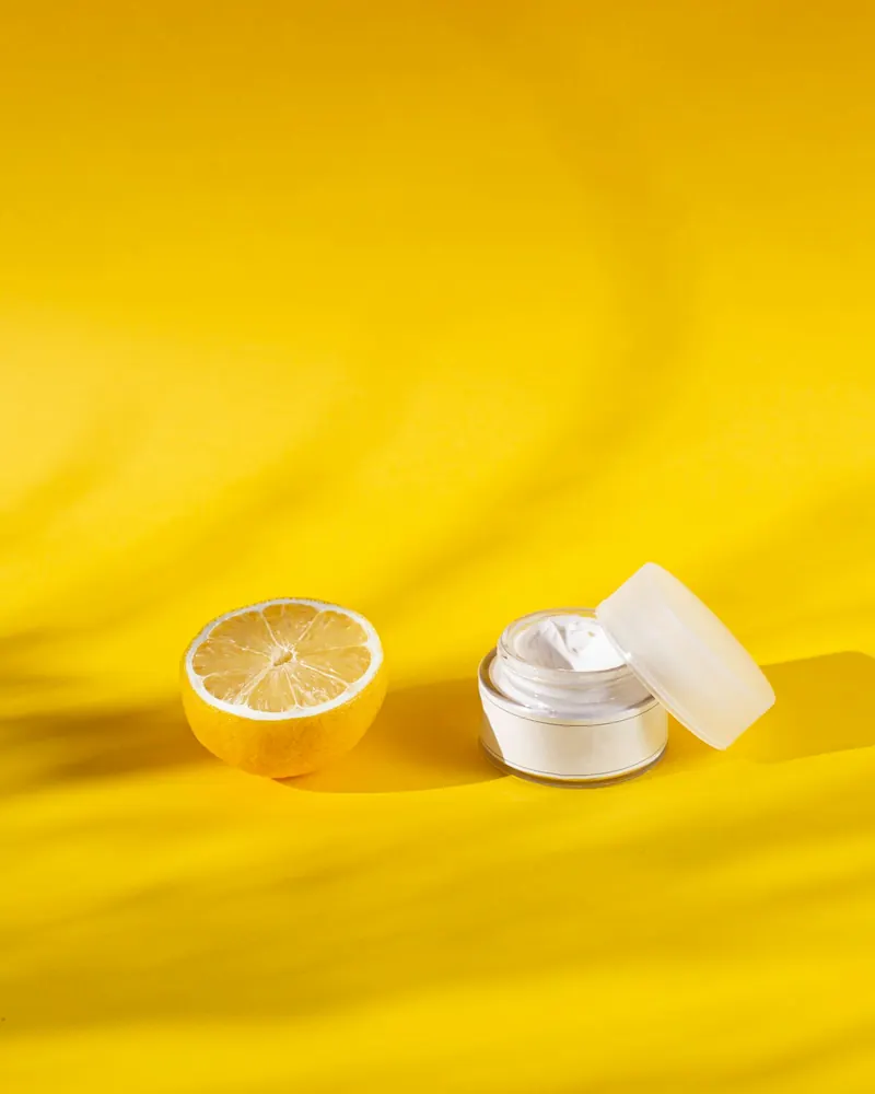 Pote de crema abierto junto a medio limón sobre fondo amarillo