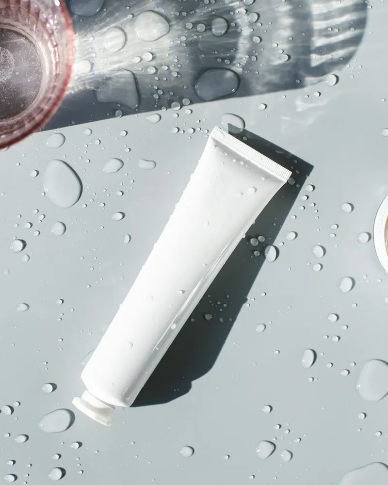Tubo blanco de gel limpiador sobre una superficie con gotas de agua