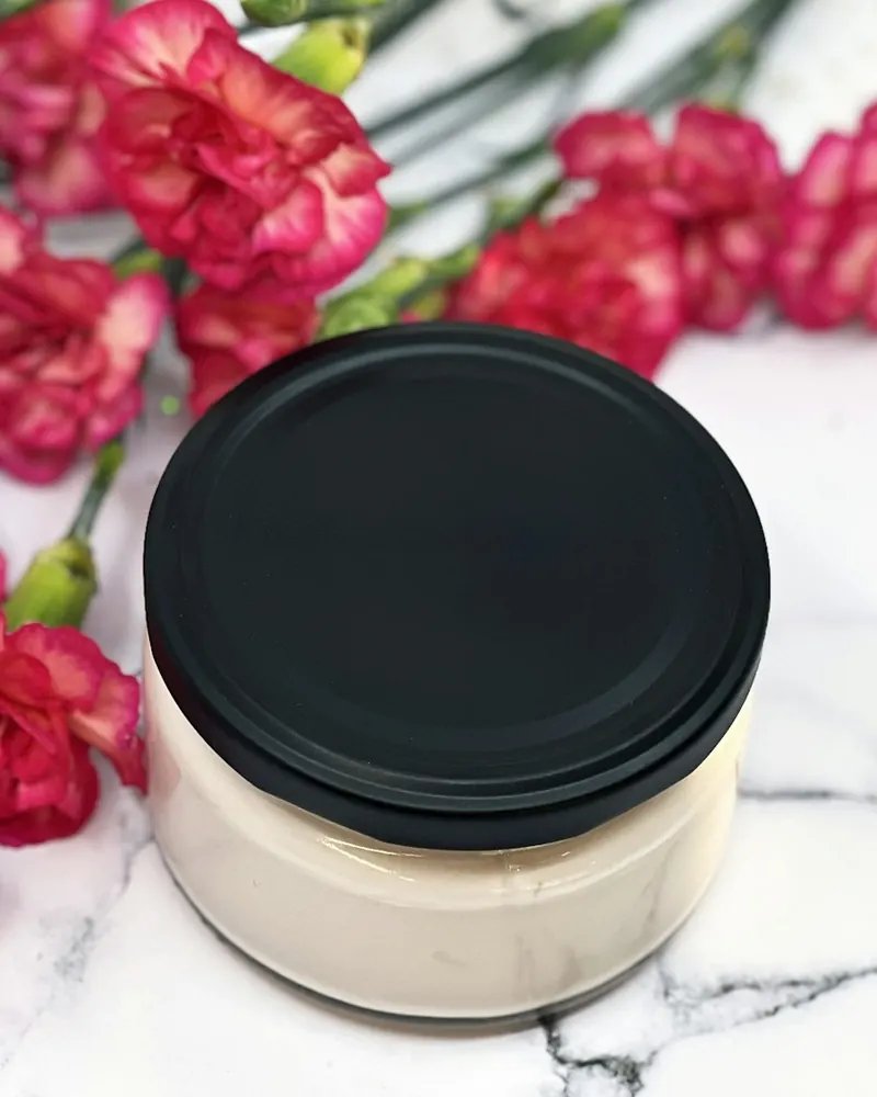 Frasco de mascarilla con tapa negra junto a claveles sobre mármol