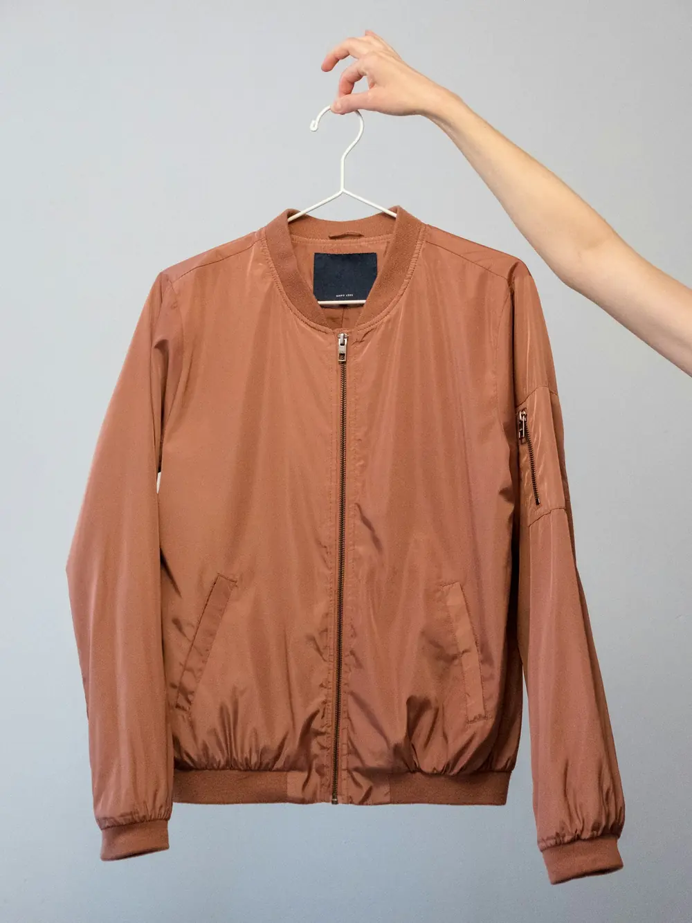 Casaca bomber color canela colgada en un gancho blanco